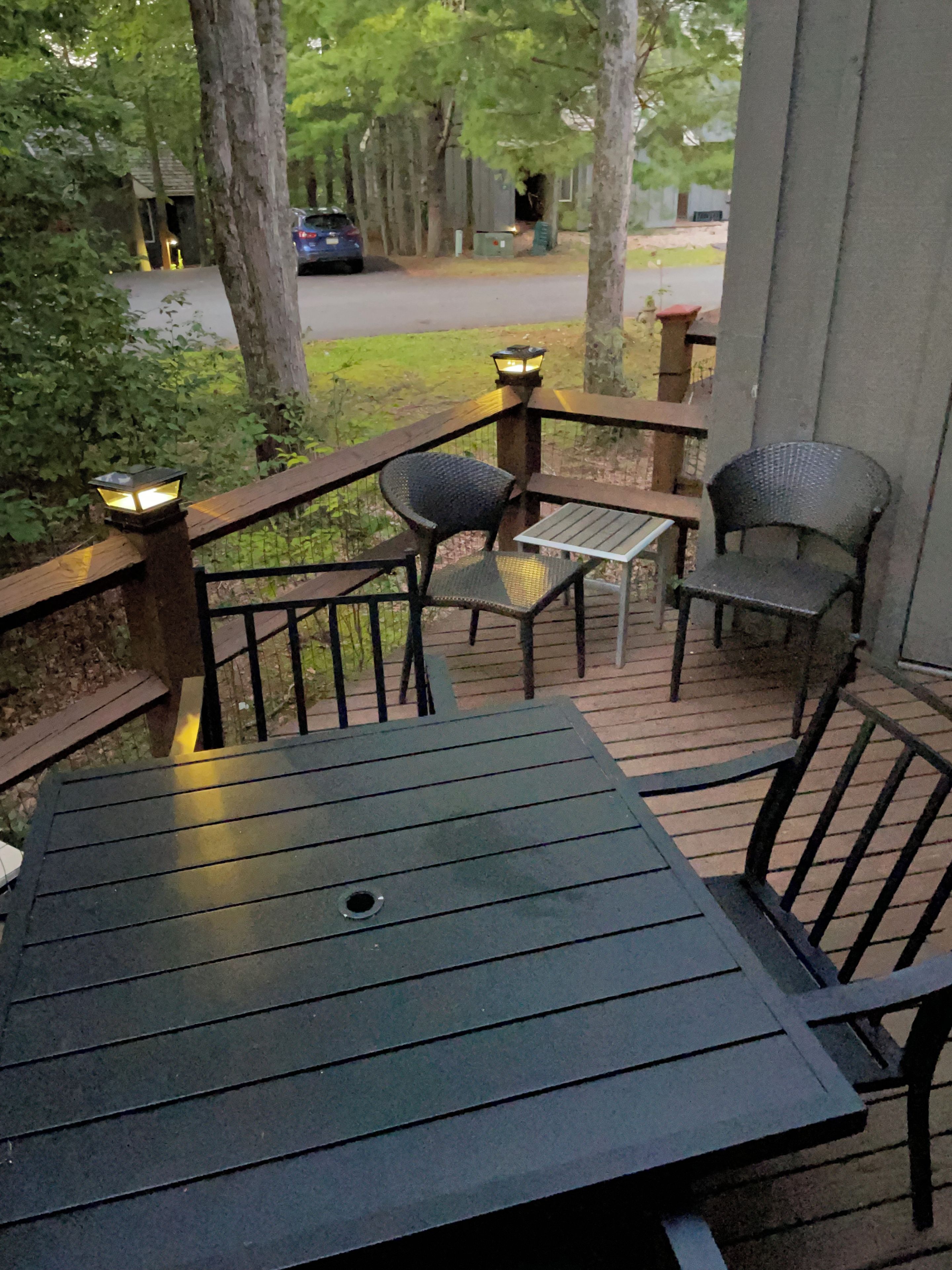 A deck with a table and two chairs, surrounded by trees and a pathway leading to a building.