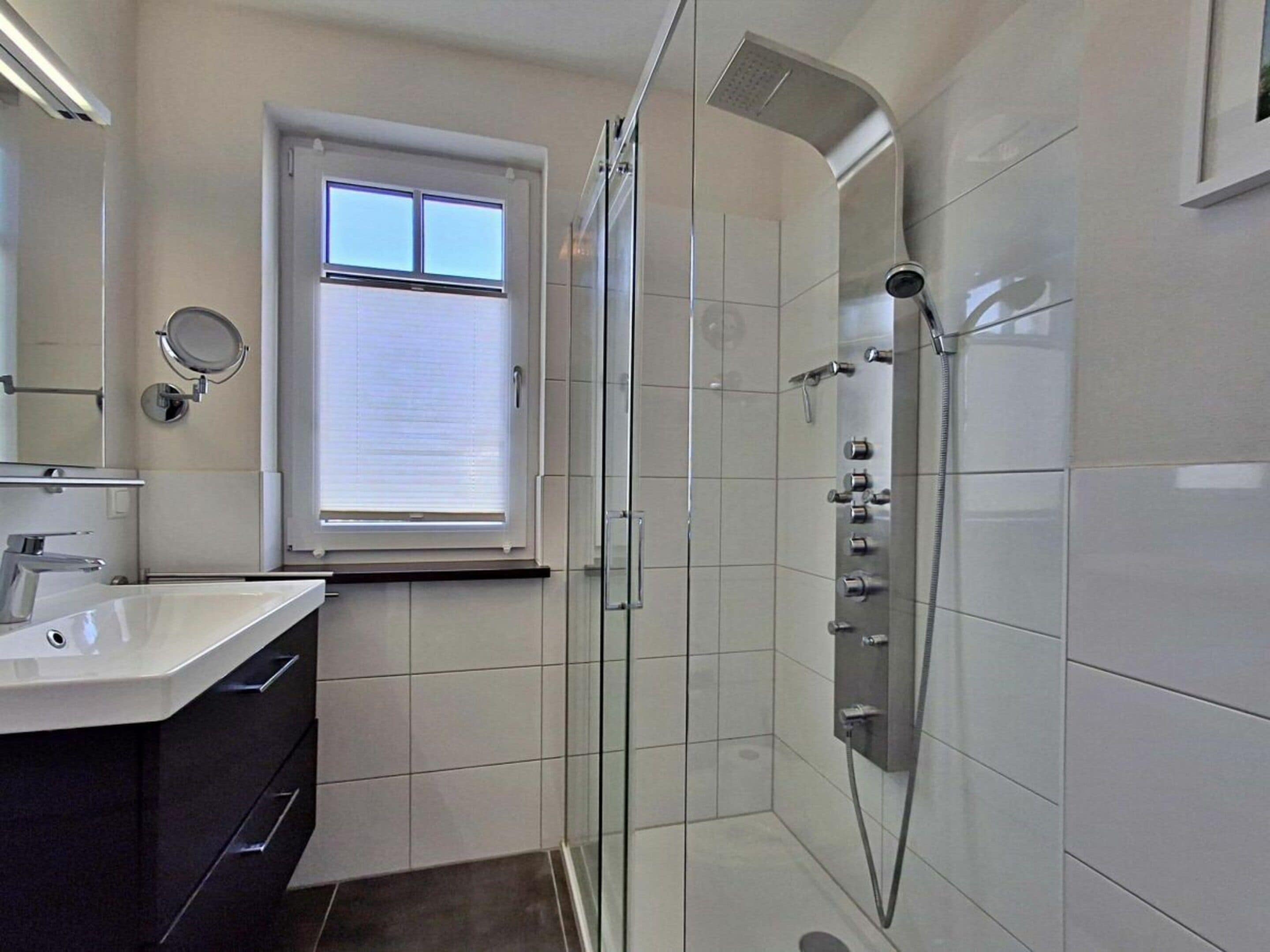A modern bathroom with a glass-enclosed shower, a vanity with a mirror, and a window with blinds.