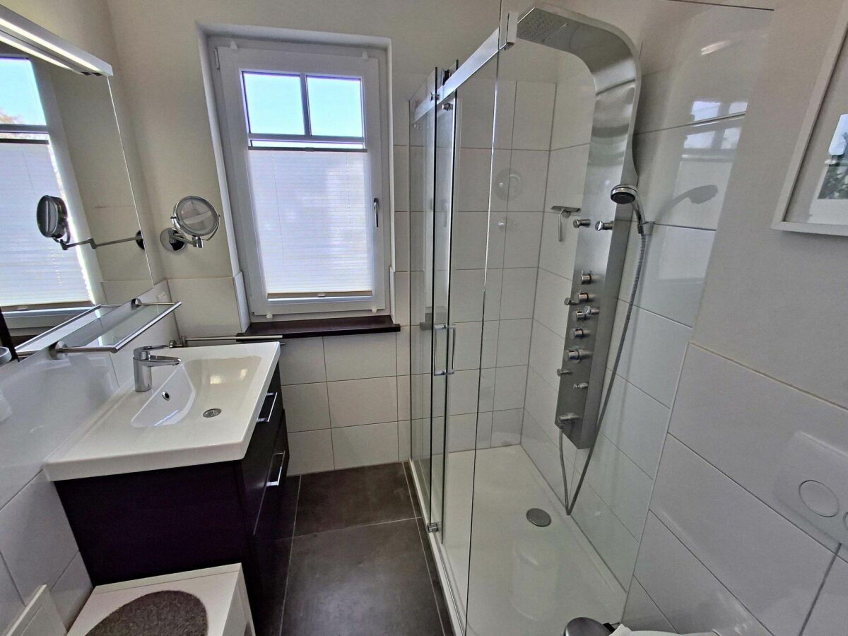 A modern bathroom with a glass-enclosed shower, a vanity with a mirror, and a window.