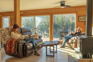 A cozy living room with a fireplace, leather sofa, and large windows offering a view of the outdoors. - Special 1-Night Stays The Gateway (Gold Bar)