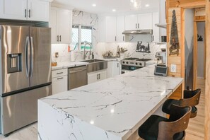 A modern kitchen with stainless steel appliances, a marble countertop, and a view of the outdoors.