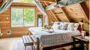 Ein gemütliches Schlafzimmer im Dachgeschoss mit einem großen Fenster, einem Bett, einem Nachttisch und einer Bank.