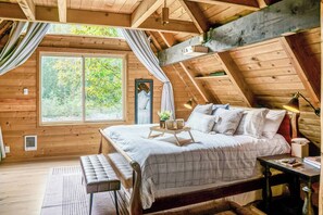 Een gezellig slaapkamer op zolder met een groot raam, een bed, een nachtkastje en een bankje.