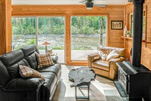 A cozy cabin interior with a leather sofa, a wooden chair, a small table, and a fireplace.