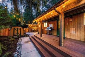 A wooden cabin with a covered patio, a grill, and string lights. - Special 1-Night Stays The Gateway (Gold Bar)