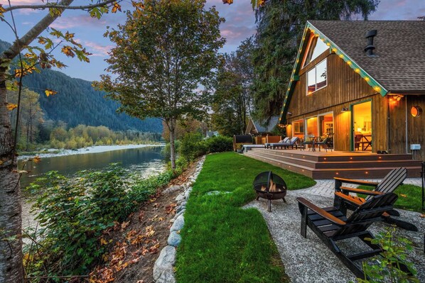 A lakeside cabin with a deck, a fire pit, and outdoor seating.