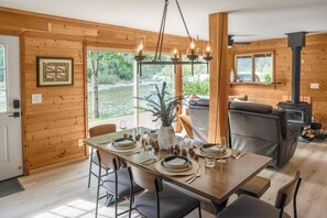 Een gezellig interieur van een blokhut met een eethoek, een open haard en uitzicht op de natuur.