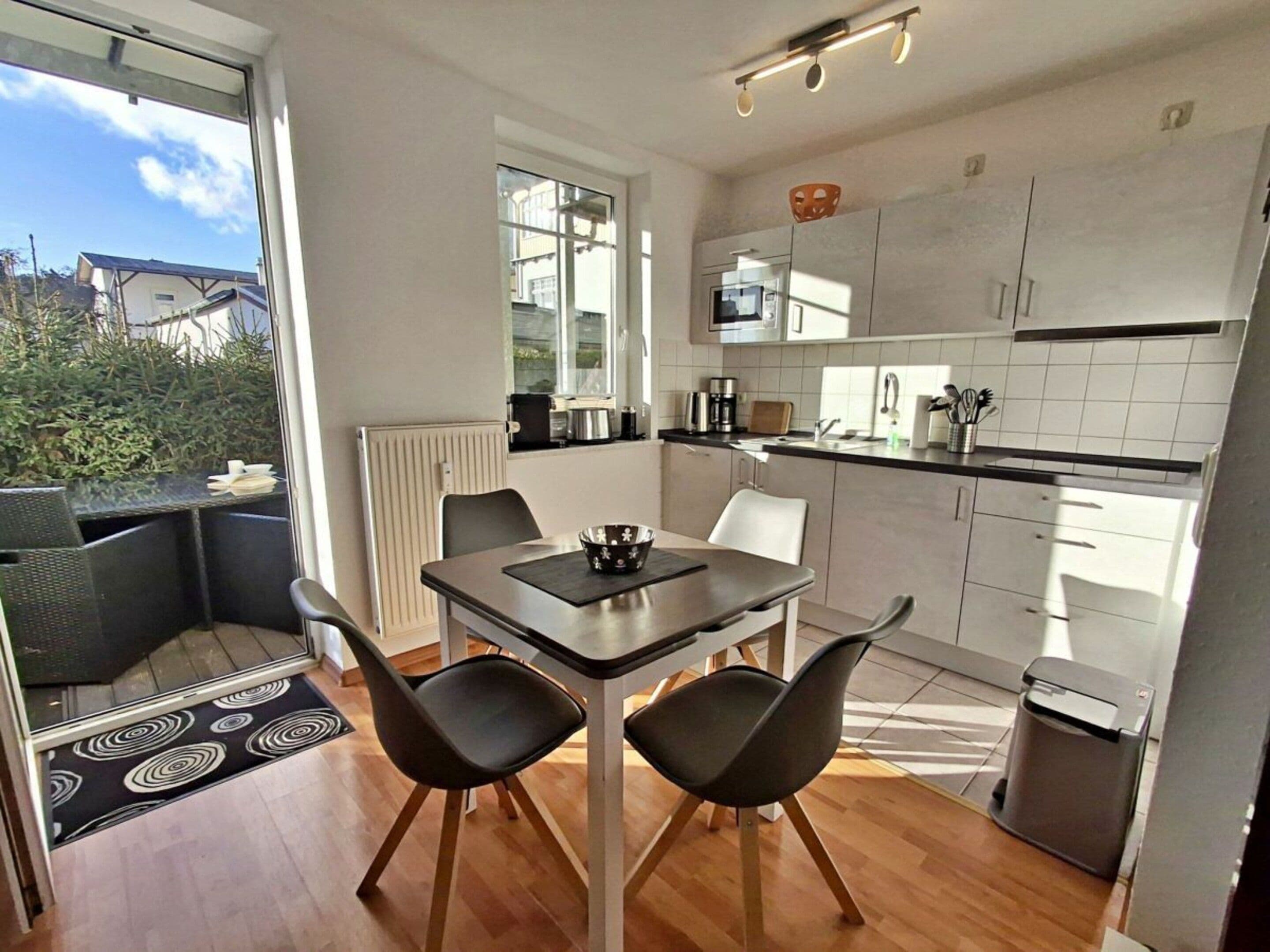 Une cuisine moderne avec des meubles blancs, une table à manger avec deux chaises et une vue sur l’extérieur.