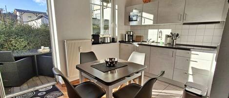 A modern kitchen with white cabinets, a dining table with two chairs, and a view of the outdoors.