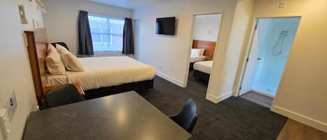 A hotel room with a bed, a desk, a chair, a TV, and a shower area.