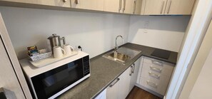 A compact kitchen with a microwave, coffee maker, and sink. - Waikato Hospital Motel (Hamilton)