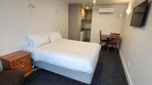 Un dormitorio con una cama, una mesita de noche de madera, una silla y un escritorio con una silla.