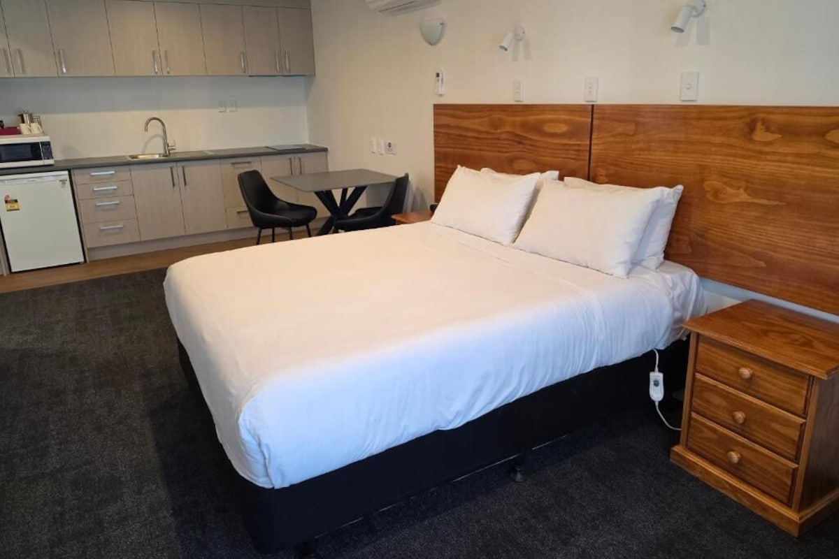 A hotel room with a bed, bedside table, and a kitchenette area.