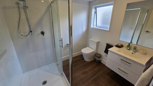 Une salle de bain avec une douche à parois de verre, des toilettes, un lavabo avec un miroir et une fenêtre.