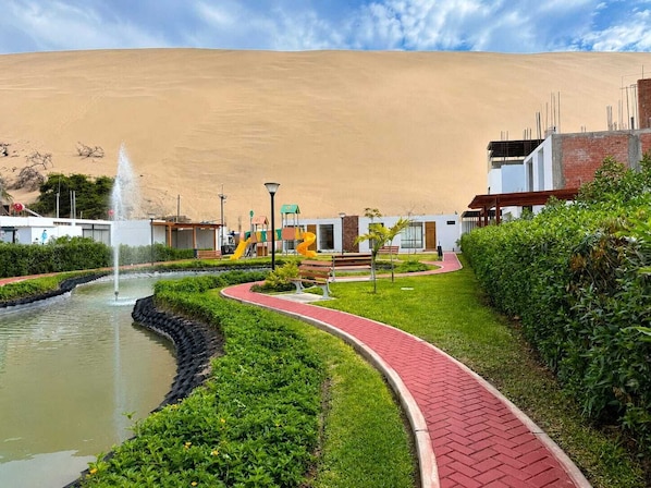 A landscaped area with a water feature, a playground, and a building with a desert backdrop.