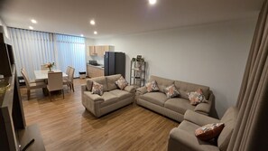 A modern living room with a sectional sofa, a dining area with a table and chairs, and a kitchen in the background. - Huacachina Oasis Dorado, Casa en Condominio Privado (Ica)