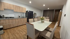A modern kitchen with wooden cabinets, a built-in oven, and a dining area with a white table and chairs. - Huacachina Oasis Dorado, Casa en Condominio Privado (Ica)