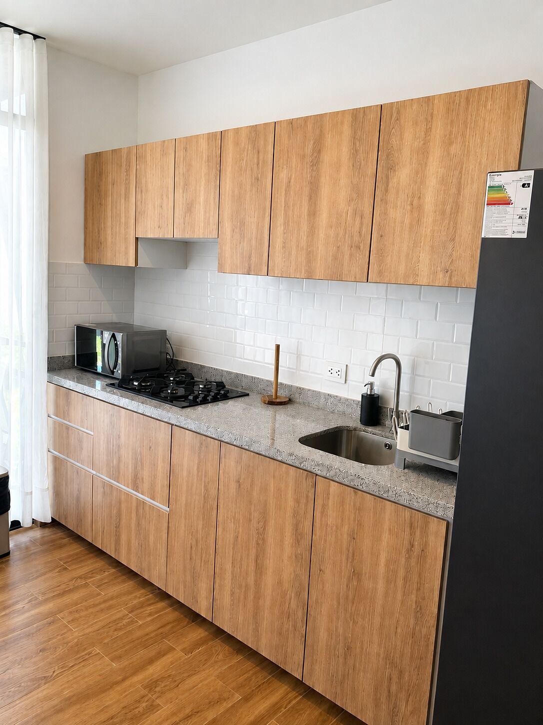 A modern kitchen with wooden cabinets, a gas stove, a sink, and a black refrigerator.