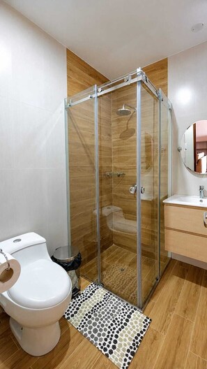 A modern bathroom with a glass-enclosed shower, a toilet, a sink, and a mirror. - Huacachina Oasis Dorado, Casa en Condominio Privado (Ica)