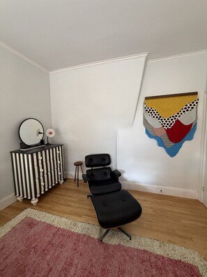 Ein Zimmer mit einem schwarzen Ledersessel, einem gestreiften Schminktisch, einem Spiegel und einem farbenfrohen Wandbild.