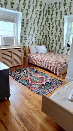 Ein Schlafzimmer mit einem Bett, einem Nachttisch, einer Kommode, einem gemusterten Teppich und einer Wand mit grün-weißen Mustern.