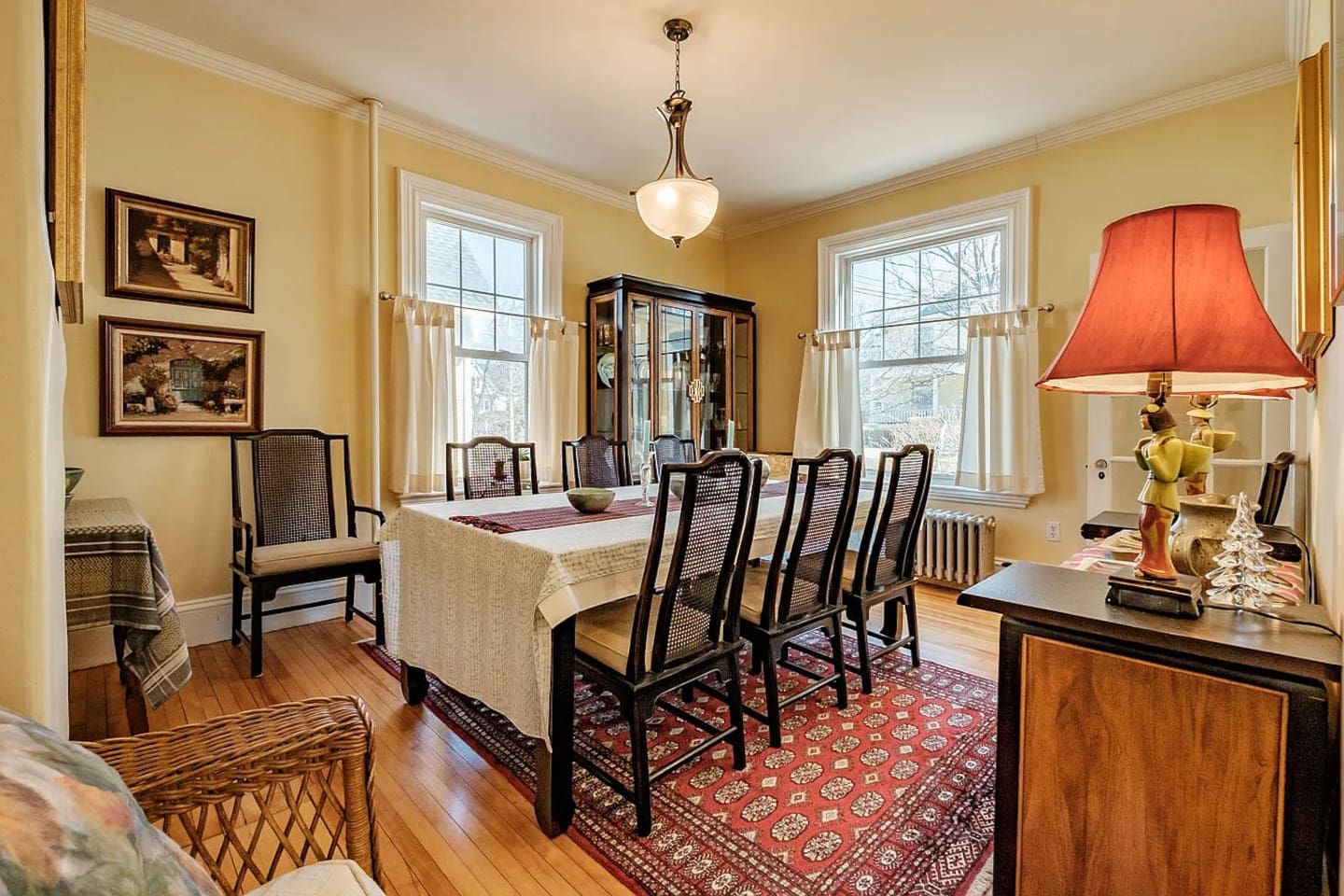 Un comedor con una mesa dispuesta para cuatro personas, rodeada de sillas, un candelabro y una alfombra roja.