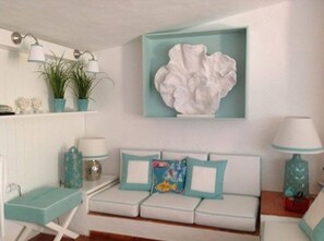 A room with a white sofa, teal cushions, a wall-mounted abstract art piece, and a teal lamp on a side table. - Charming home in the Algarve near the best golf courses (Olhos de Água)