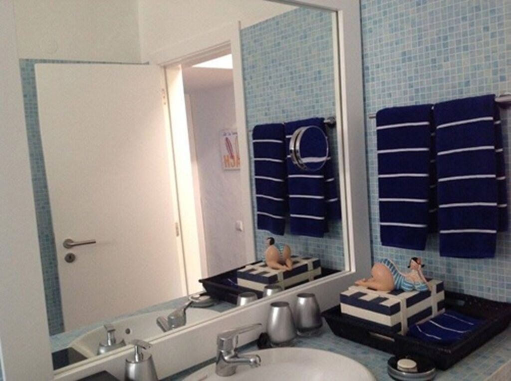 Une salle de bain avec un grand miroir, un lavabo et un porte-serviettes muni de plusieurs serviettes.
