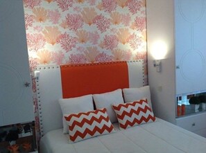 Ein Schlafzimmer mit einem Bett, zwei Kissen, einem Kopfteil, einer Wandleuchte und einer Wandtapete mit Muster.