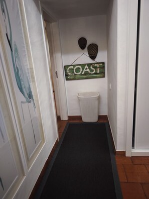 A hallway with a black mat, a wicker basket, and a 'COAST' sign on the wall. - Charming home in the Algarve near the best golf courses (Olhos de Água)