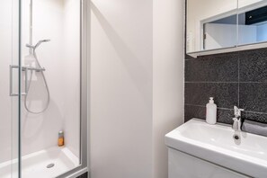Un baño moderno con cabina de ducha de vidrio, un lavabo blanco y una pared de azulejos oscuros.