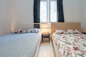 A bedroom with two beds, a window with curtains, a bedside table with a lamp, and a radiator. - Stylish Apartment With Modern Amenities (Antwerp)