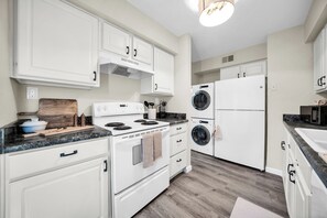 A modern kitchen with white cabinetry, a stove, a microwave, and a built-in washing machine. - The perfect gem in the heart of Phoenix Biltmore! (Phoenix)