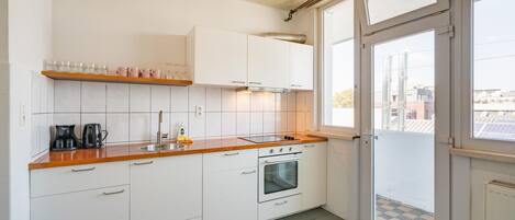 Uma cozinha com armários brancos, bancada de madeira, pia, cafeteira e forno.