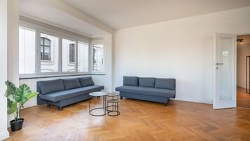 A spacious living room with a grey sofa set, a small round table, and a potted plant.