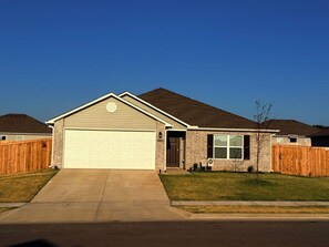A single-story house with a garage, a front yard, and a wooden fence. - Ride to Bella Vista 3/4 Mi · Bike Garage · Fenced Yard, Dogs · Fireplace/grill (Pea Ridge)