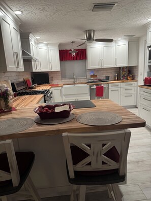 A modern kitchen with white cabinetry, a wooden countertop, and a central island with seating. - Beautiful beach house getaway (New Port Richey)