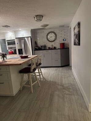 A modern kitchen with white cabinetry, a wooden countertop, and a dining area with chairs. - Beautiful beach house getaway (New Port Richey)
