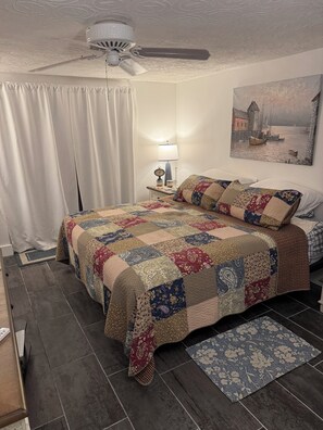 A bedroom with a bed, a nightstand, a ceiling fan, a painting, and a window with curtains. - Beautiful beach house getaway (New Port Richey)