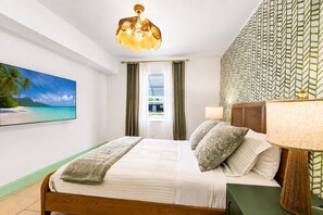 A hotel room with a bed, a television, a window with curtains, a patterned wall, and a ceiling light fixture. - Vrbo Property (Treasure Island)