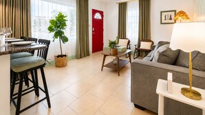 Un salon moderne avec un canapé, une table à manger accompagnée de chaises, une porte rouge et une grande fenêtre avec des rideaux.