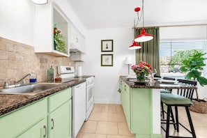 A modern kitchen with green cabinets, a granite countertop, a built-in oven, and a dining area with a bar stool. - Treasure Island Getaway | Walk to the beach | Pet-friendly (Treasure Island)