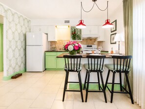 A modern kitchen with green cabinets, a white refrigerator, a central island with chairs, and pendant lights. - Treasure Island Getaway | Walk to the beach | Pet-friendly (Treasure Island)
