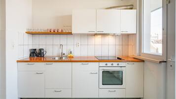 A compact kitchen with white cabinets, a stainless steel sink, a built-in oven, and a window providing natural light.