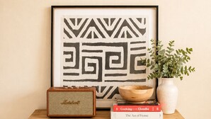 A wooden cabinet with two doors, a framed abstract artwork, a vintage radio, a bowl, a potted plant, and a book titled 'Cooking con Claudia'.