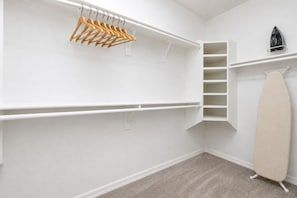 A walk-in closet with wooden hangers, a shelf unit, and a stand-up ironing board.