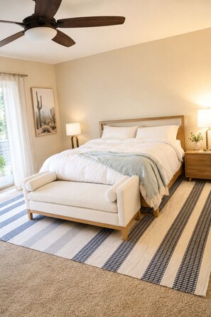 Een slaapkamer met een bed, nachtkastjes, een plafondventilator en een raam met gordijnen.