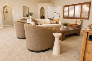 A living room with a beige sofa, two armchairs, a coffee table, and a decorative vase.