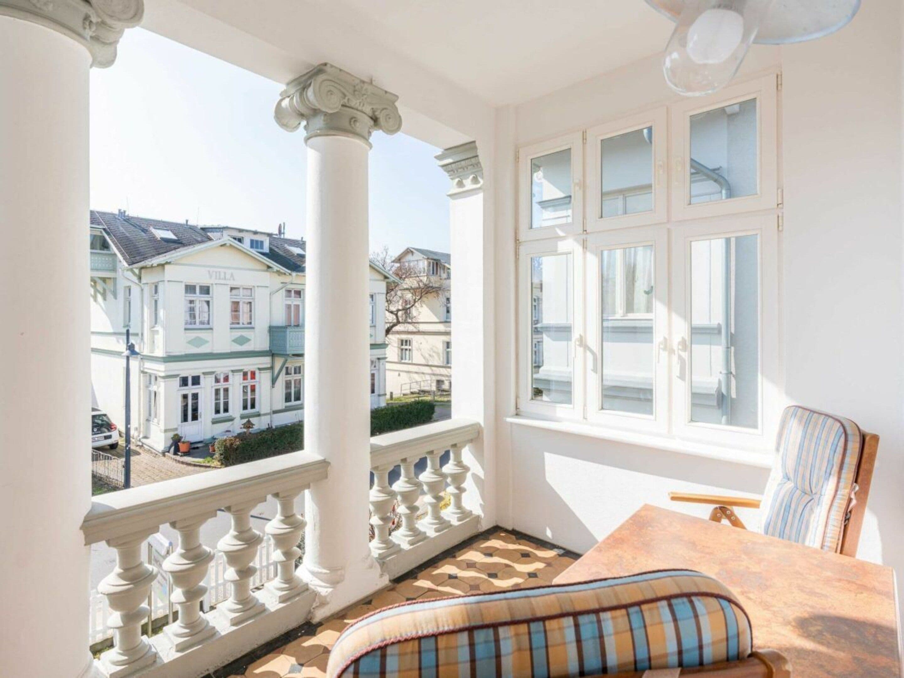 Un balcon donnant sur des immeubles, une table avec un coussin et une chaise.