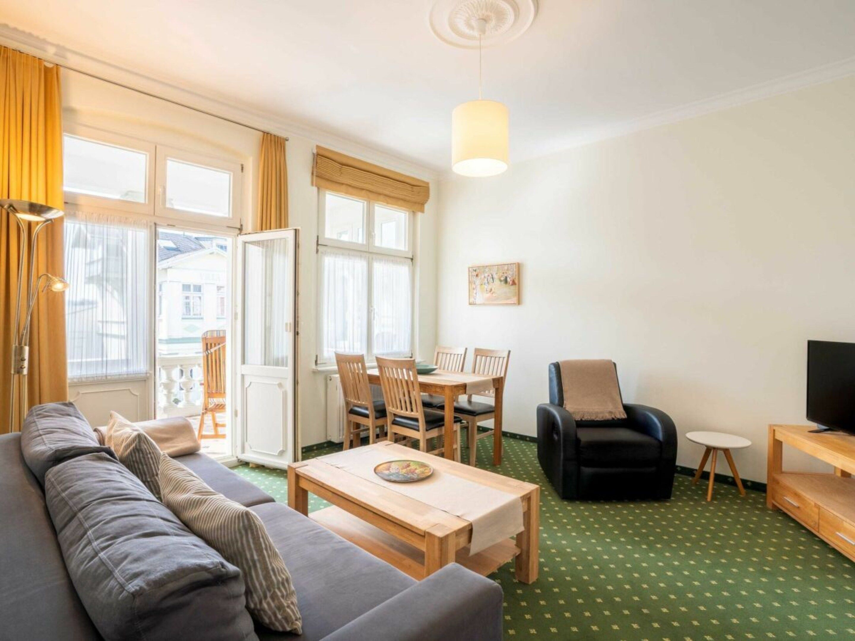 A living room with a sofa, a dining table with chairs, a television, and a patterned carpet.